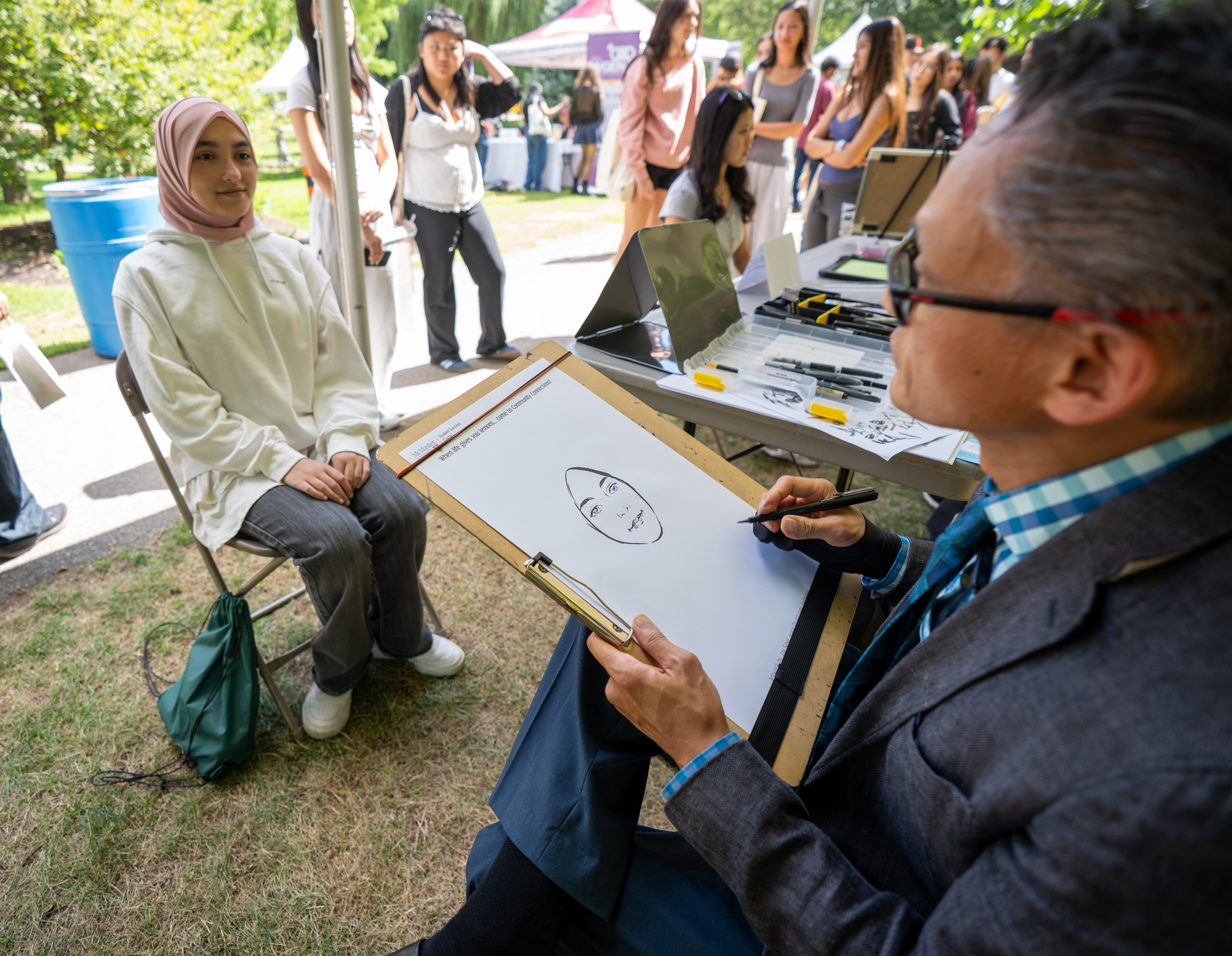 A caricaturist works on a drawing of a woman seated in front of him during Community Connections at Welcome Week 2025