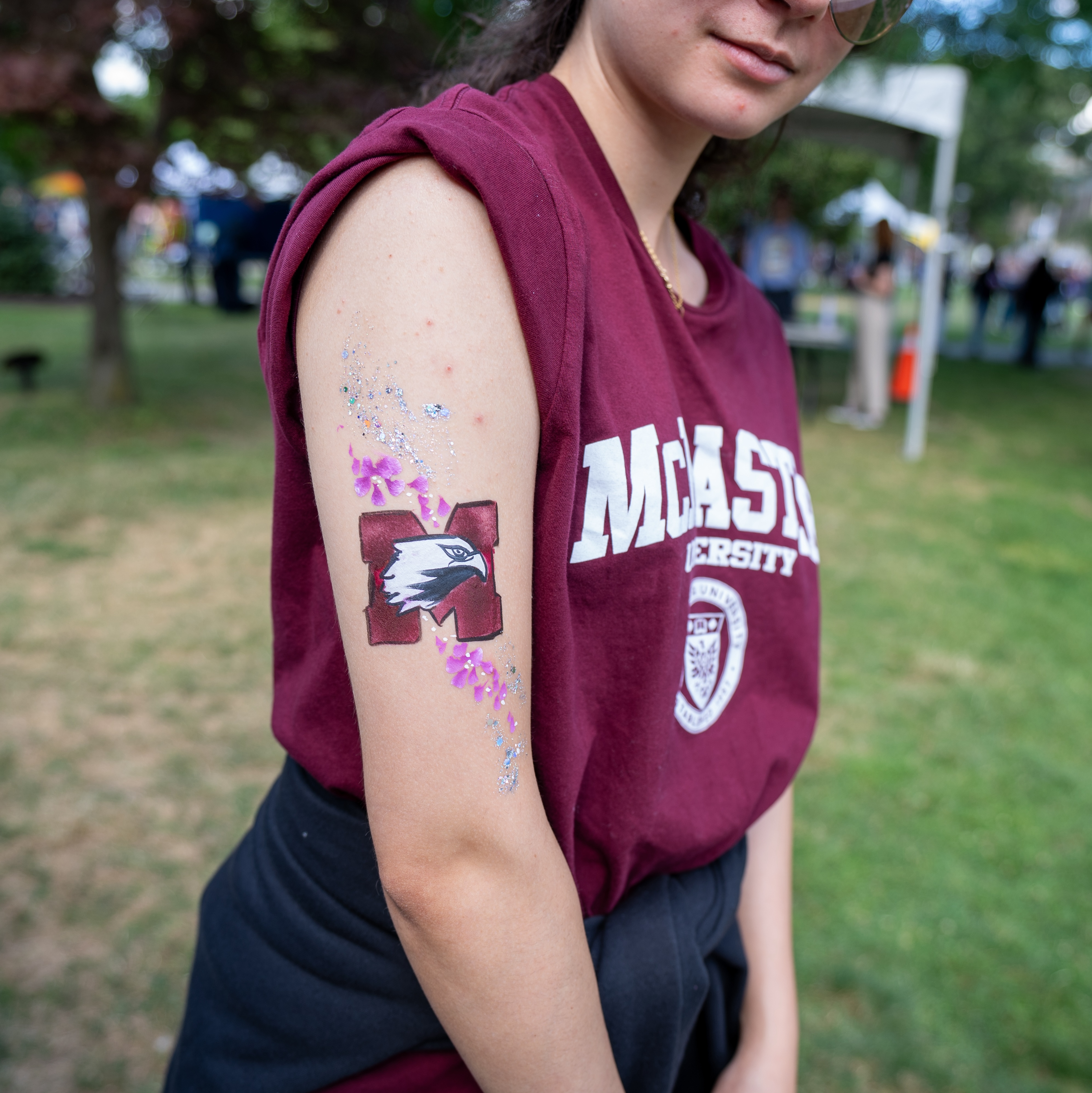 A student in a McMaster Tshirt shows off their Marauders logo painted on their biceps.