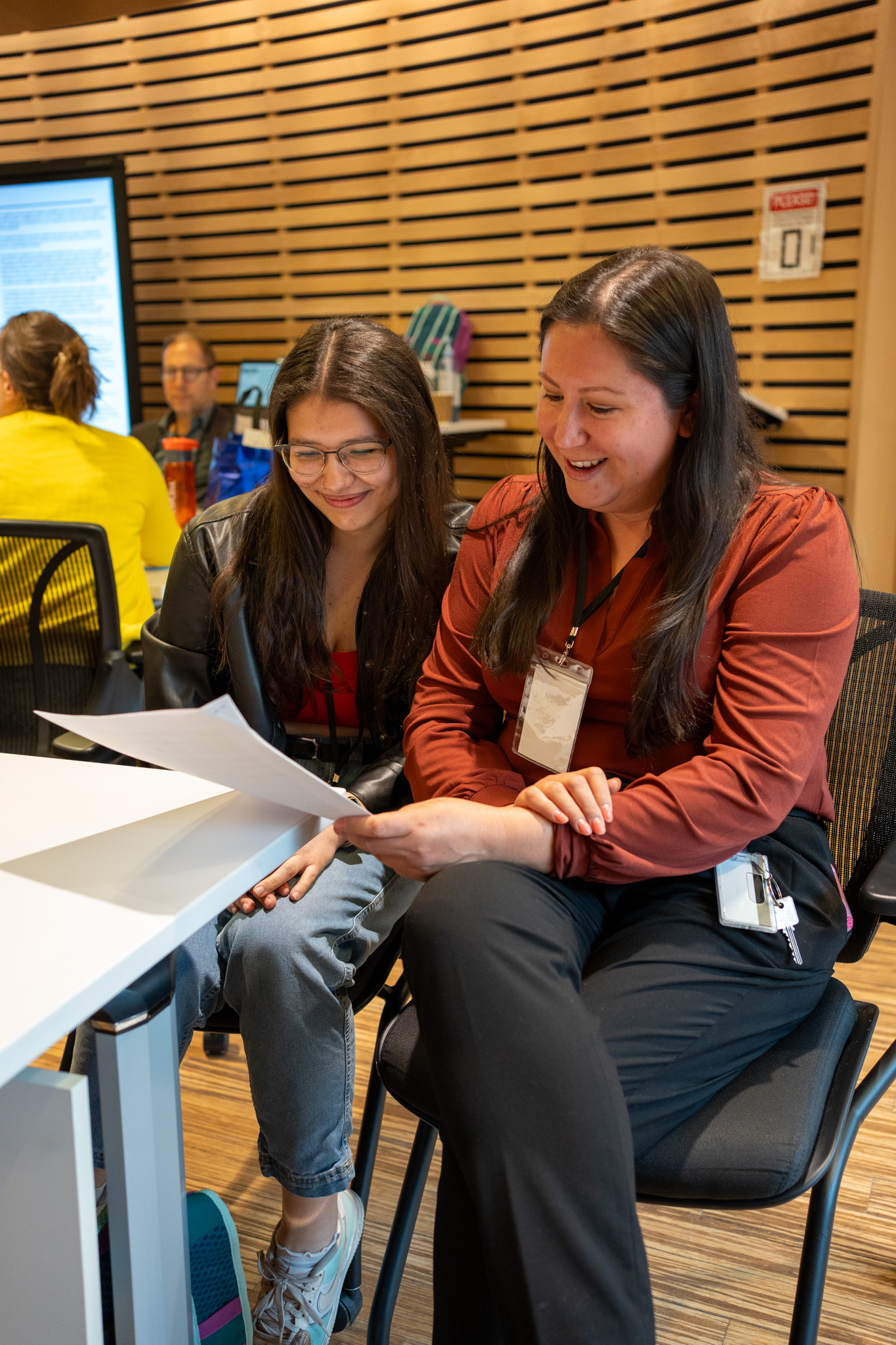 Two women sit at a table, looking at a piece of paper.