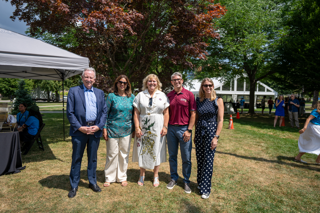 Five people in dress clothes stand outside on a summer's day, posing for the camera. 