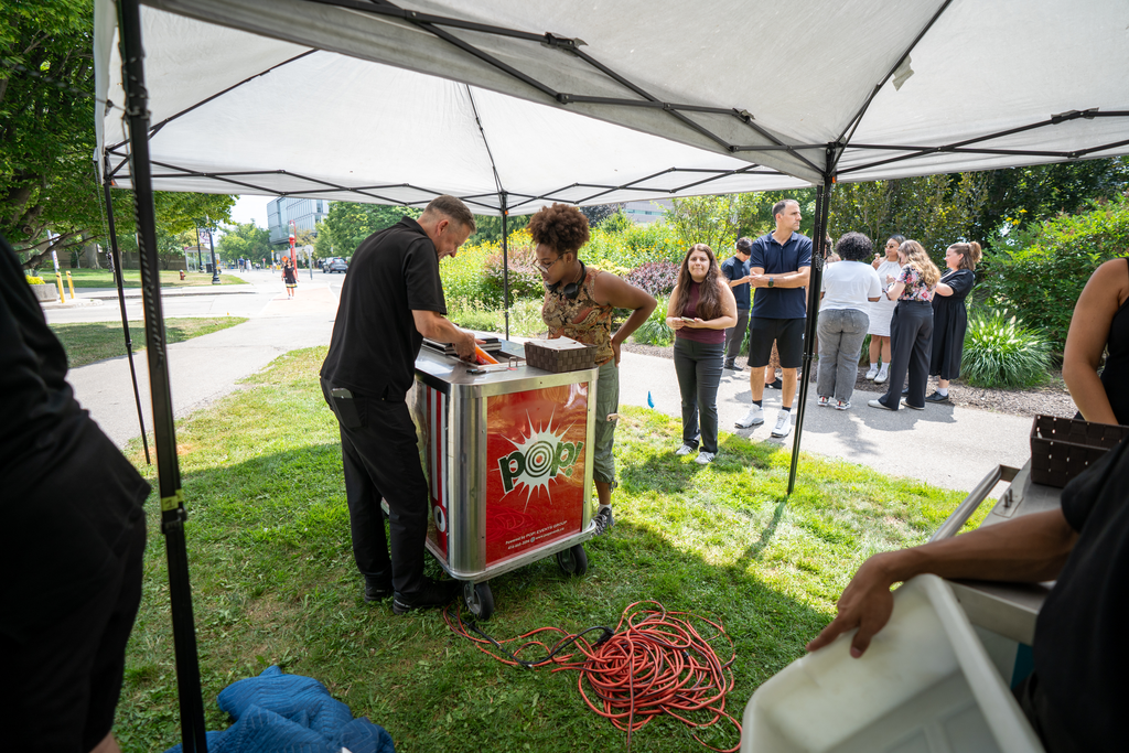 A shade tent sits over a freezer, where a man is pulling out frozen treats for a line of people.