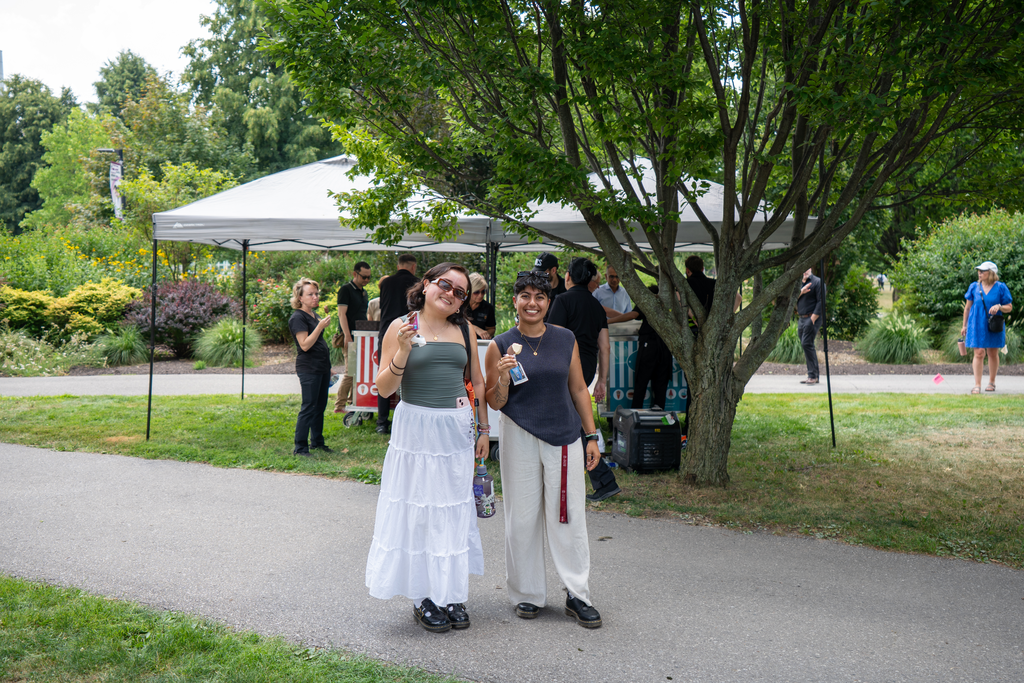 Two people stand on a sidewalk outside, eating ice cream.