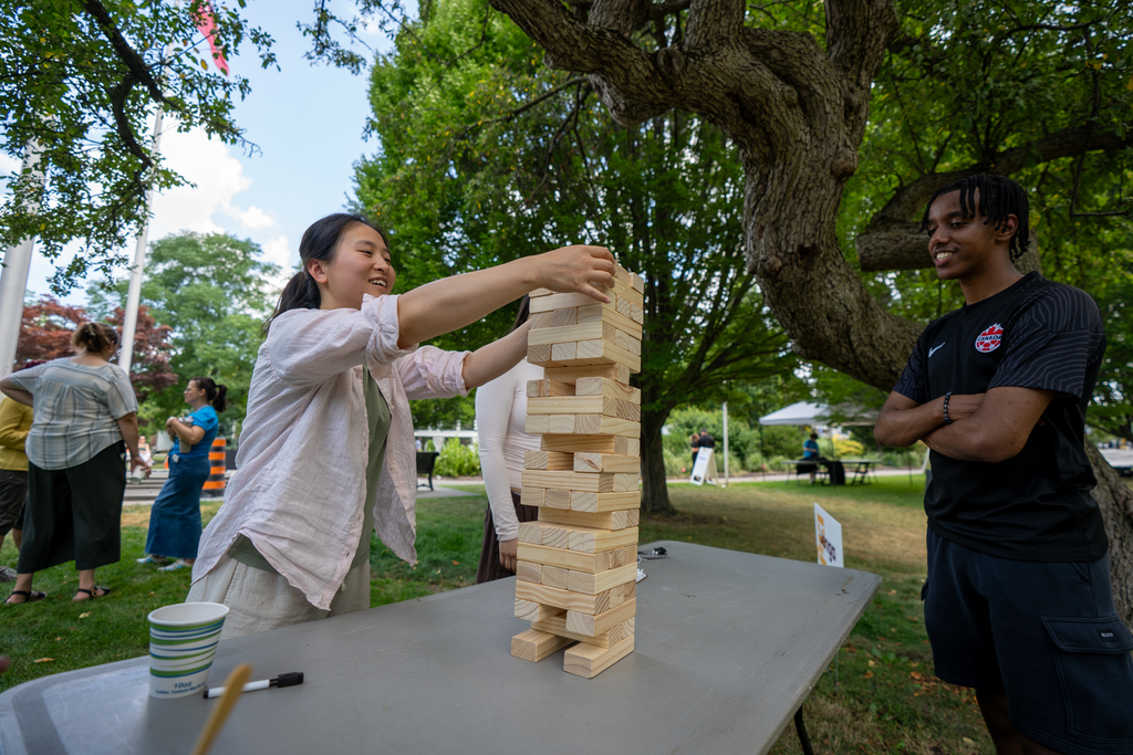 Two people play Jenga on a table outdoors.