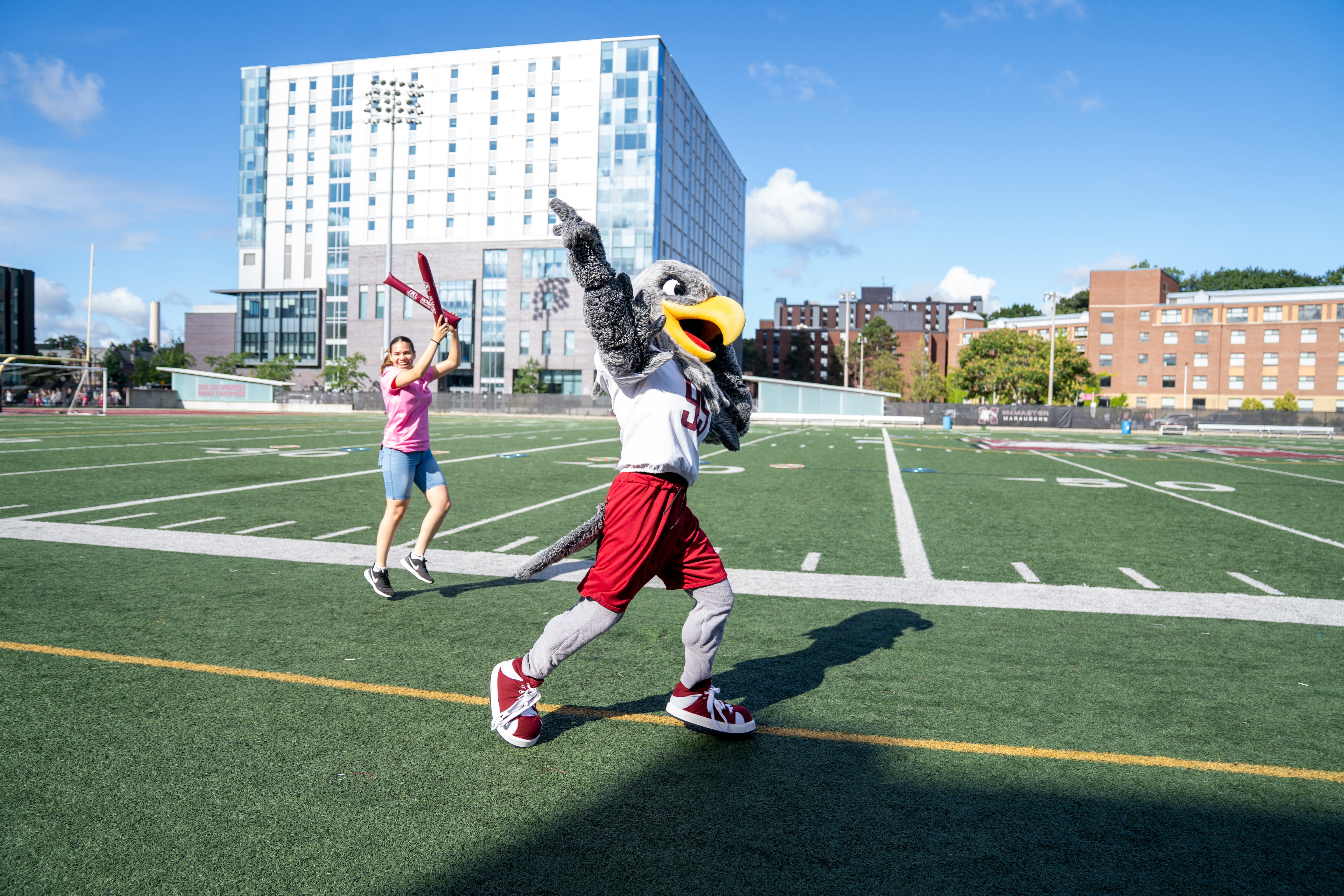 Mac the Marauder runs across the stadium turf, followed by a fan.