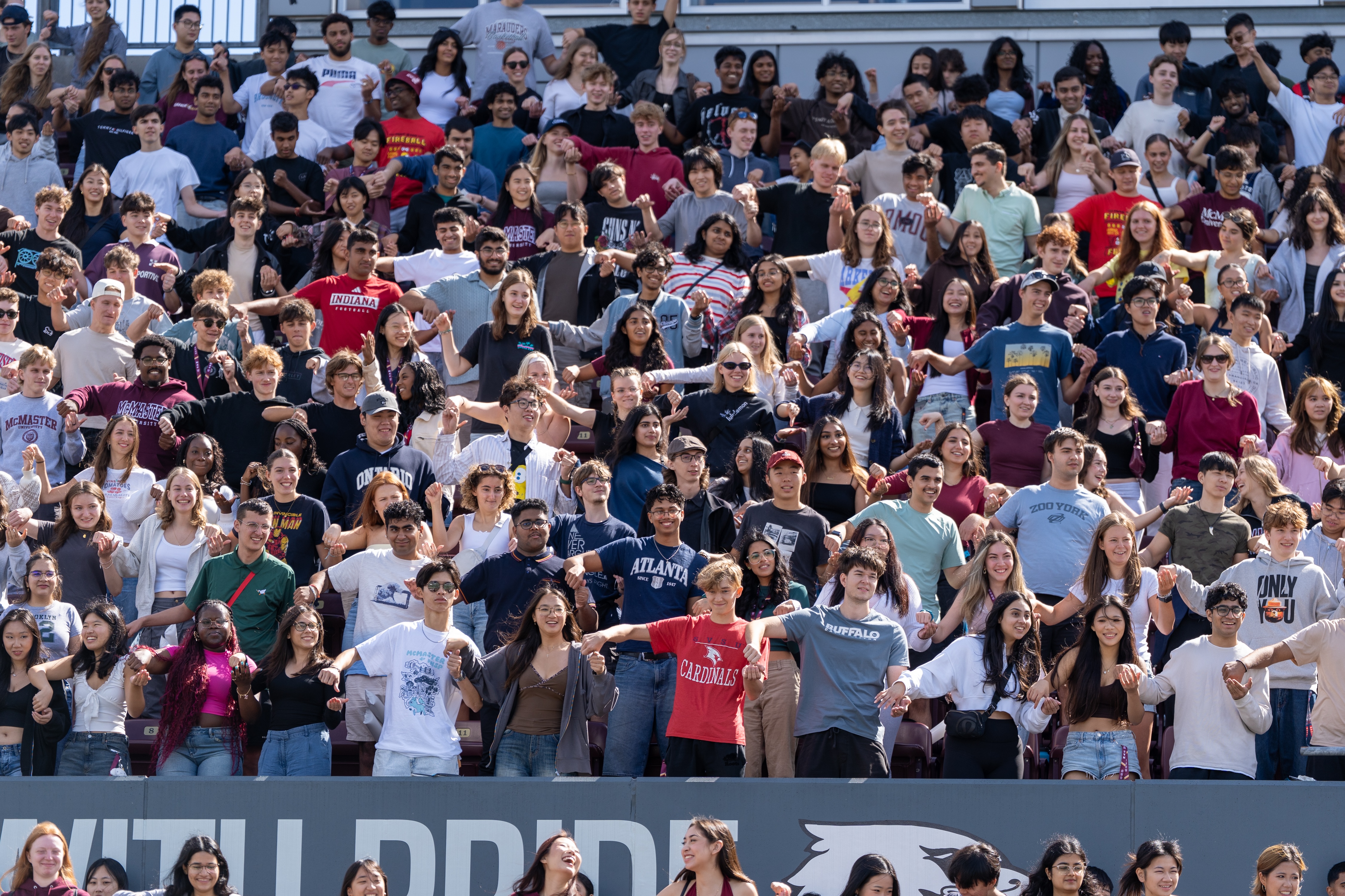 Students clasp hands in the stands at the McMaster Welcome at the stadium during welcome week 2025