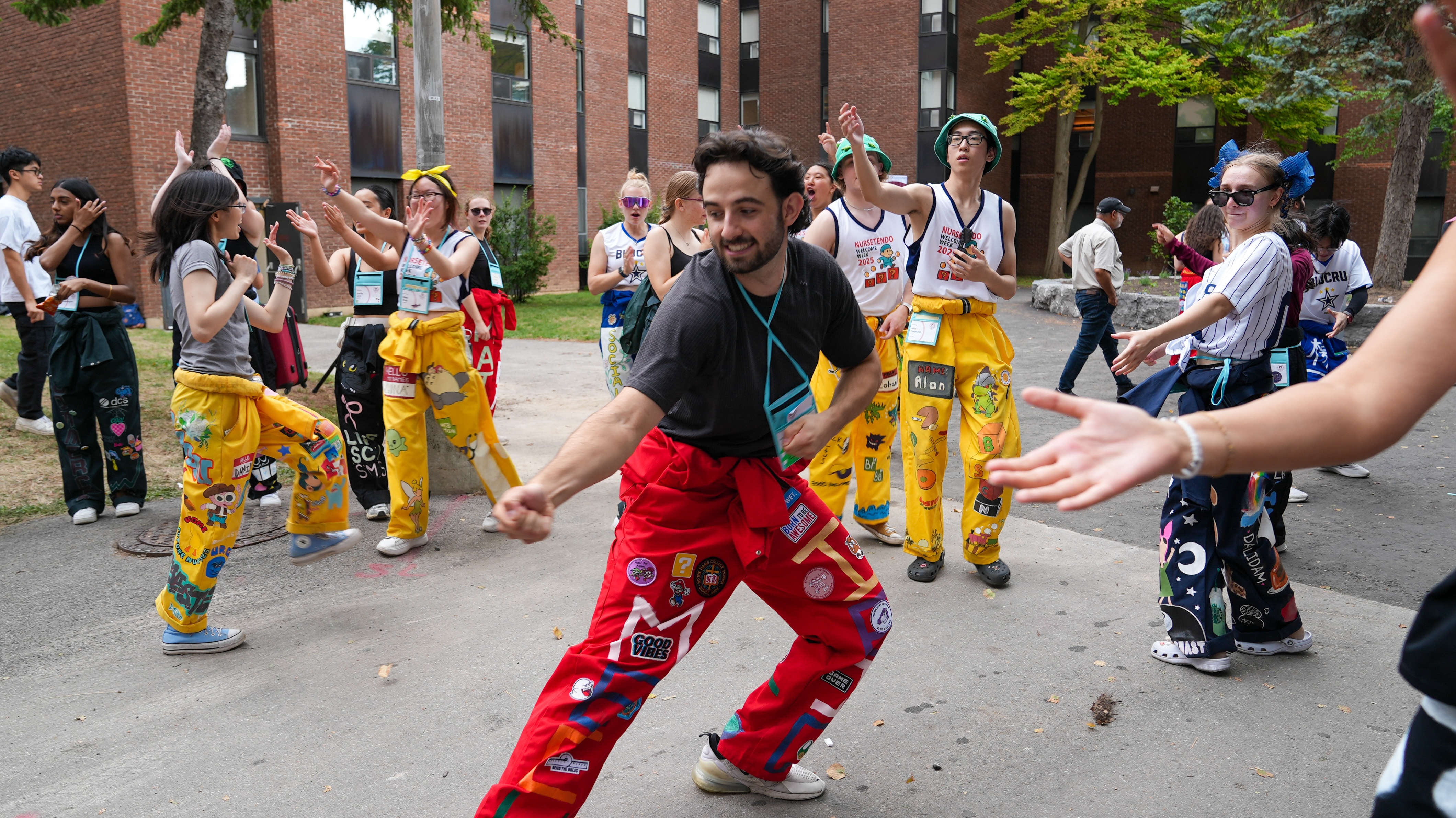 A Welcome Week rep in a red [Engineering] jumpsuit pretends to pull in a first-year's car with an invisible rope while reps in other colours cheer and clap