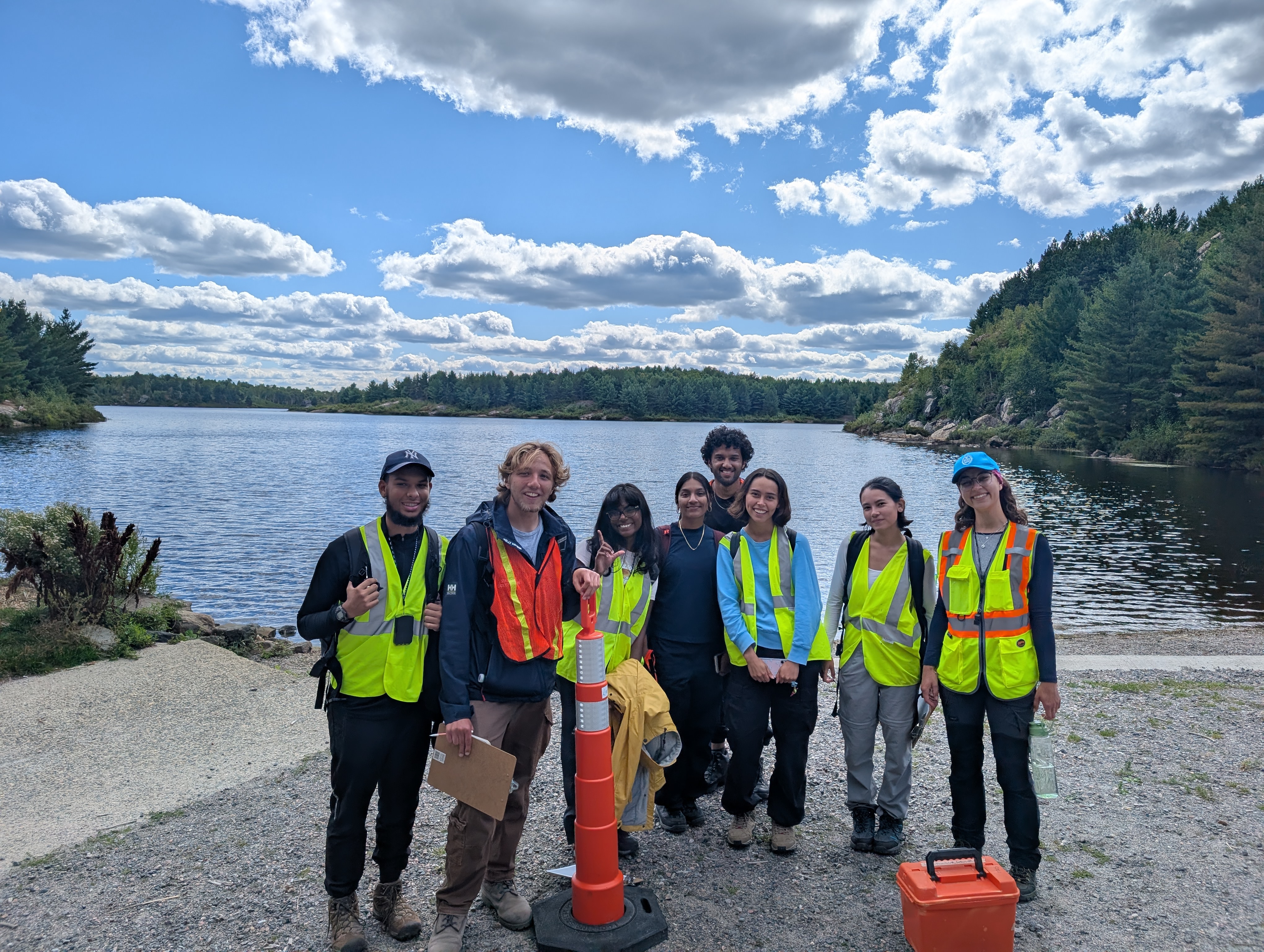 Several people in hi-vis vests stand on a rocky outcrop overlooking a lake. 