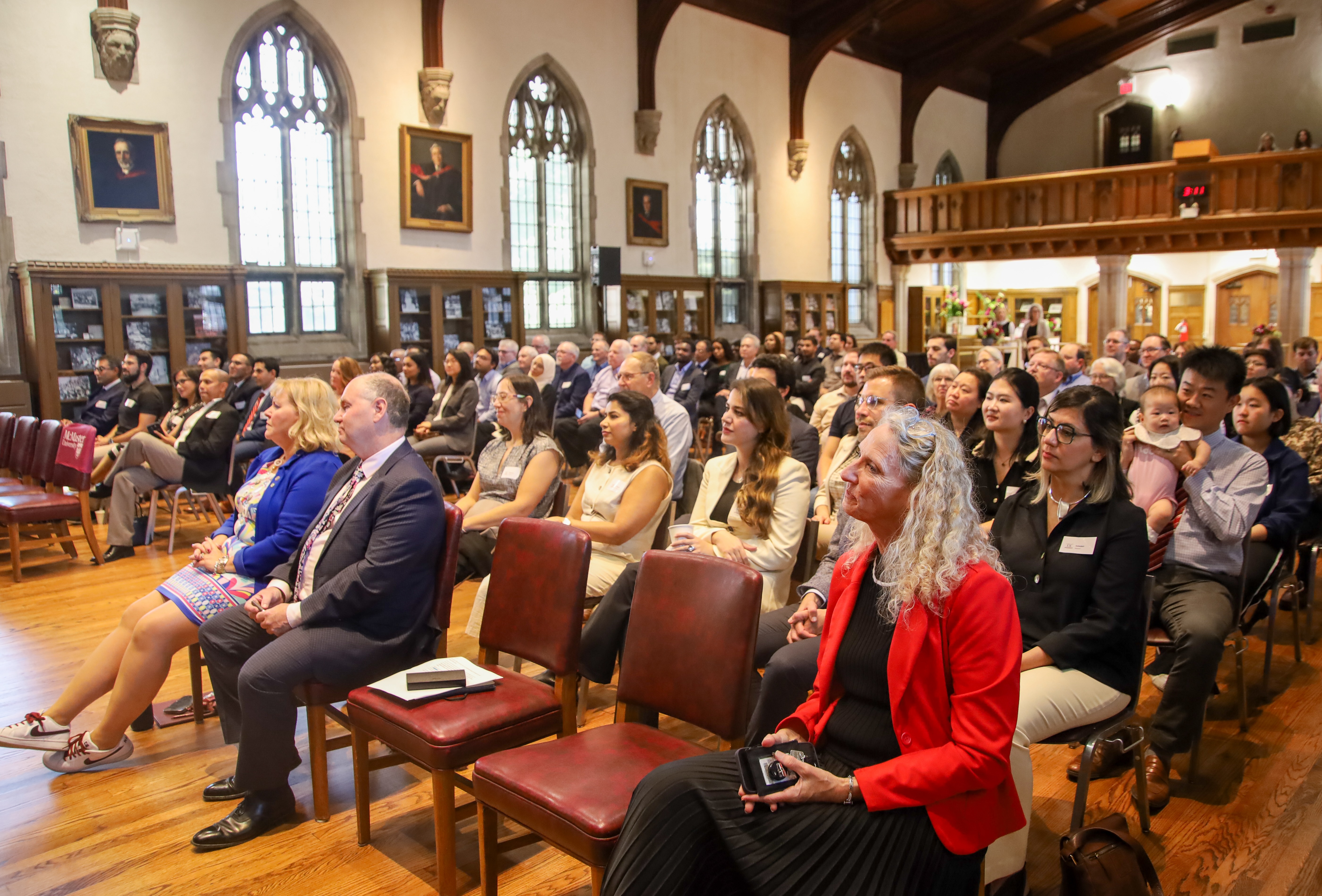 Rows of people sit in Convocation Hall, watching the panel discussion on stage.