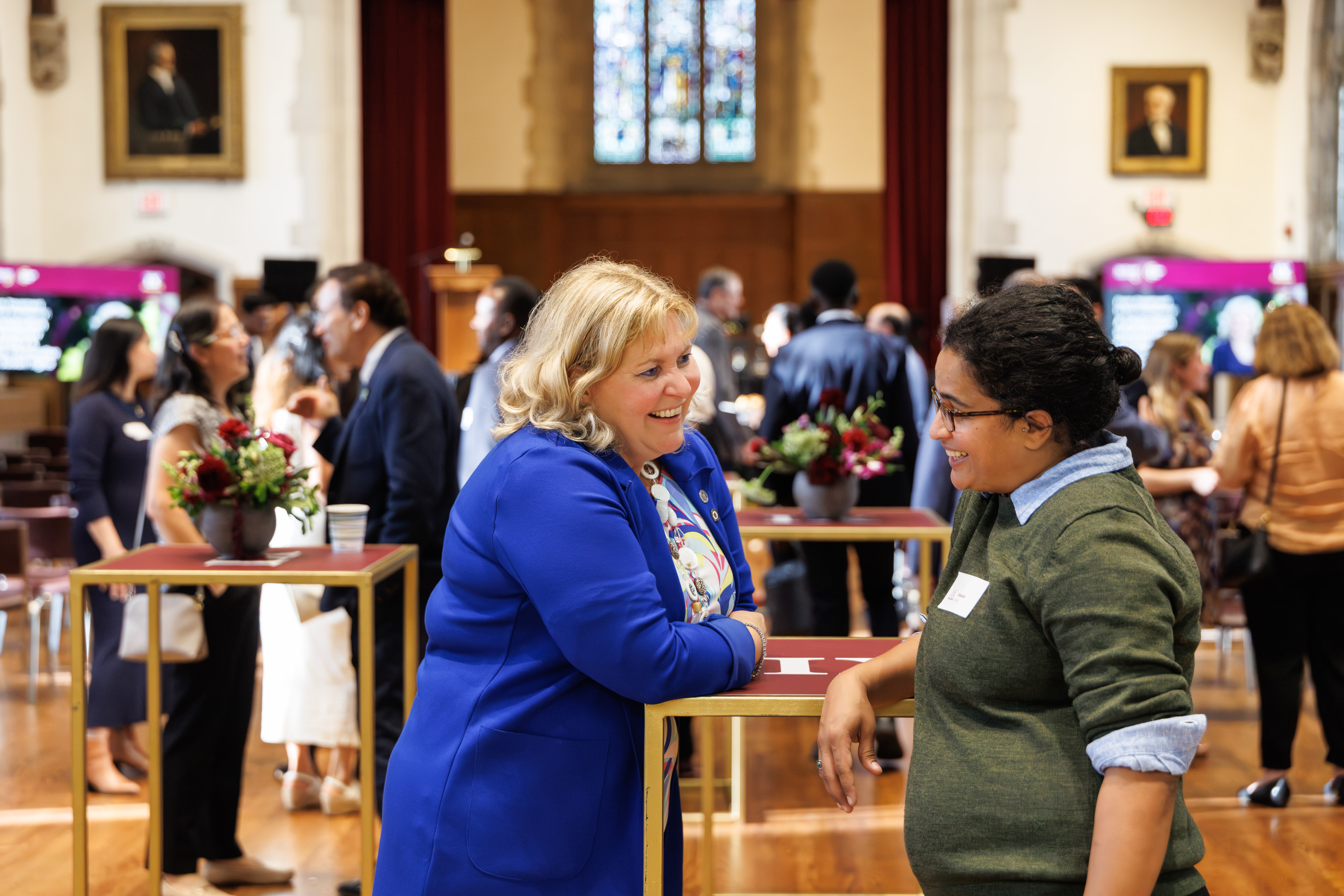 Susan Tighe and a student lean on a bar-height table, smiling and chatting.