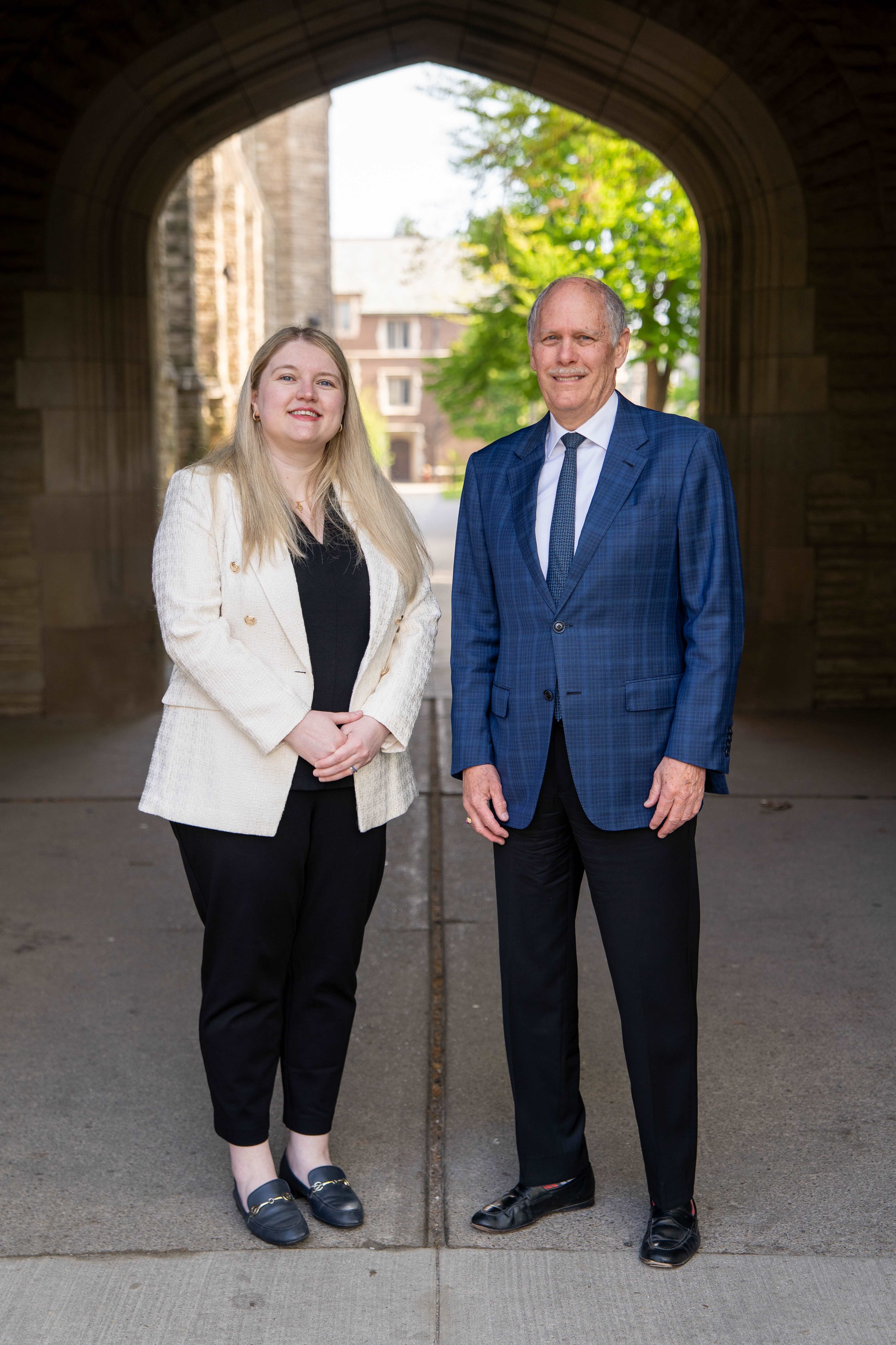Two people in business clothes stand under a stone archway.