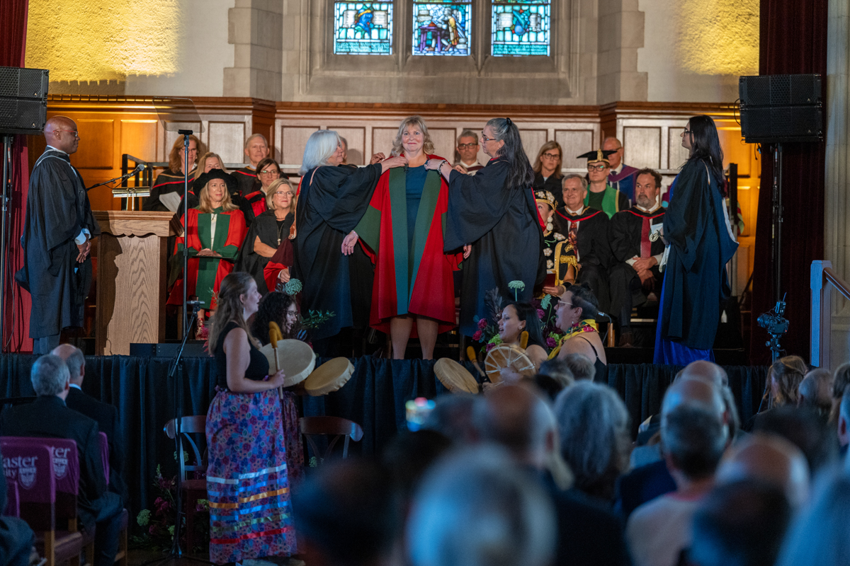 Two people help Susan Tighe remove the doctoral robes she is wearing over her blue dress.