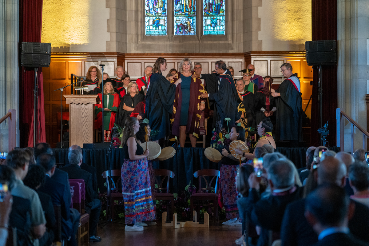 Piper Plavins and Bhagwati Gupta help Susan Tighe put on the official robes of McMaster University’s president.