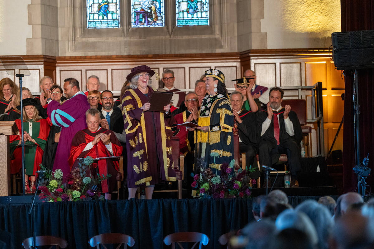 Santee Smith and Susan Tighe smiling after Smith handed Tighe a folder containing the university charter on stage in Convocation Hall.