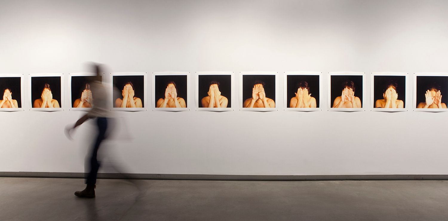 An art installation of a series of photographs, each showing a person with their hands in front of their face. 