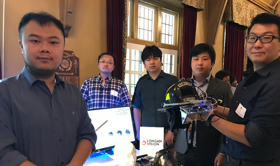 Five men stand around a table. One is holding a fire fighter's helmet.