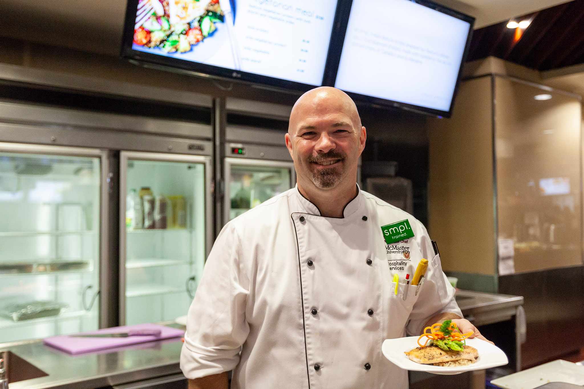 Chef holding a plant-based dish behind an eatery counter.