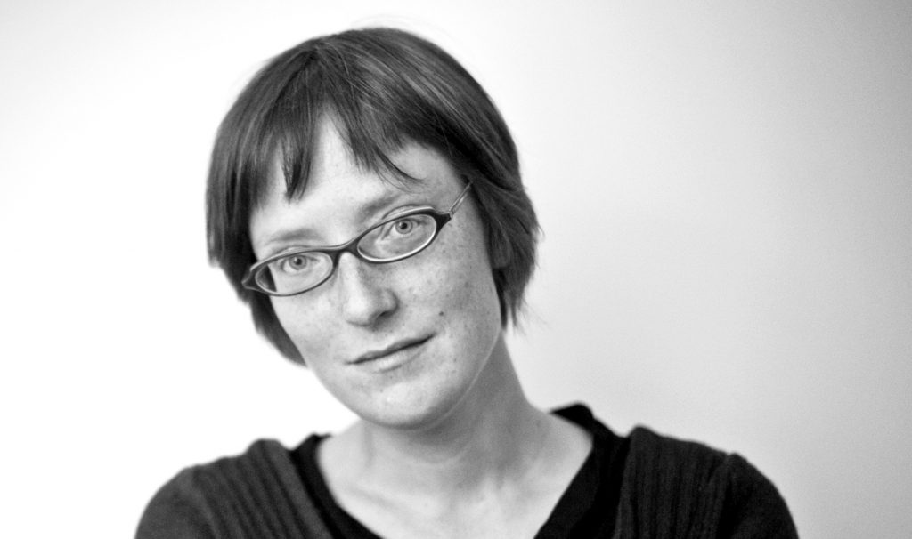 A black and white photo of a woman with short hair and glasses looking at the camera