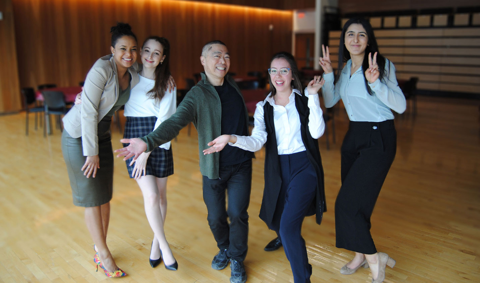 Four women and one man pose theatrically while smiling