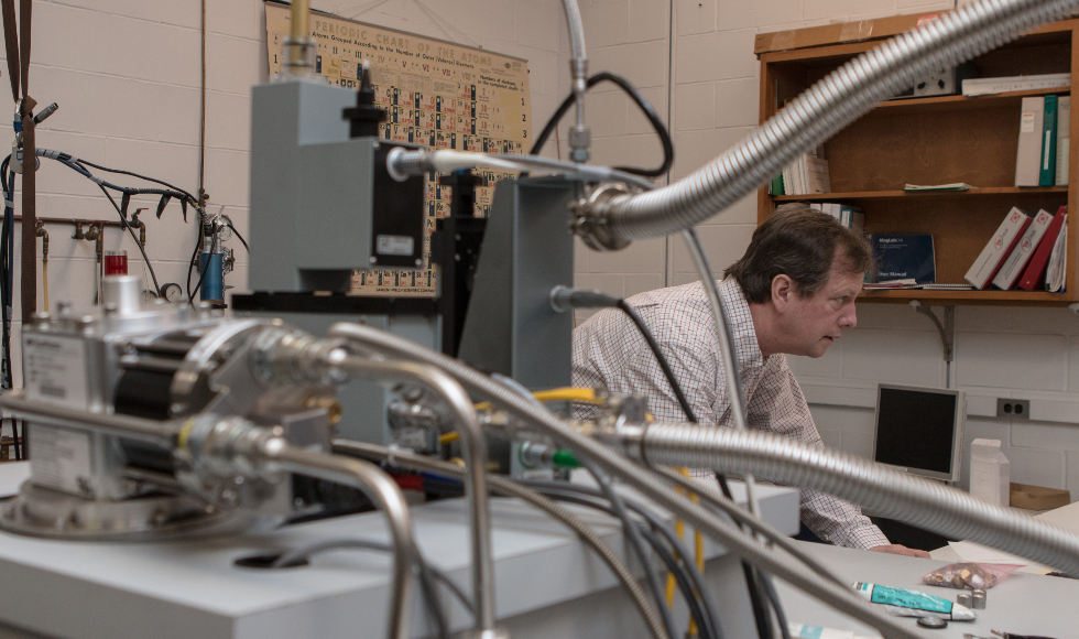 A man stands in a lab behind a tangle of wires