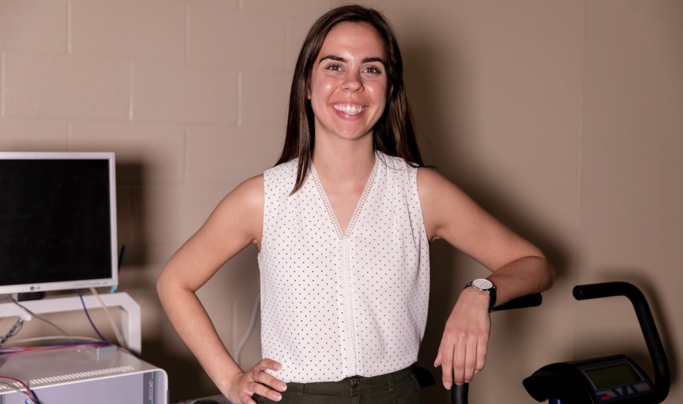 Teaching Assistant Michelle Ogrodnik stands beside an exercise bike