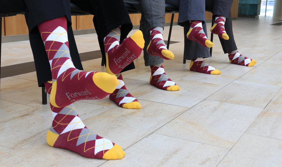 Close up of four pairs of feet wearing maroon and gold argyle socks