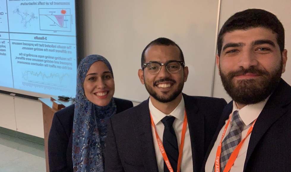 Three smiling people face the camera in a classroom