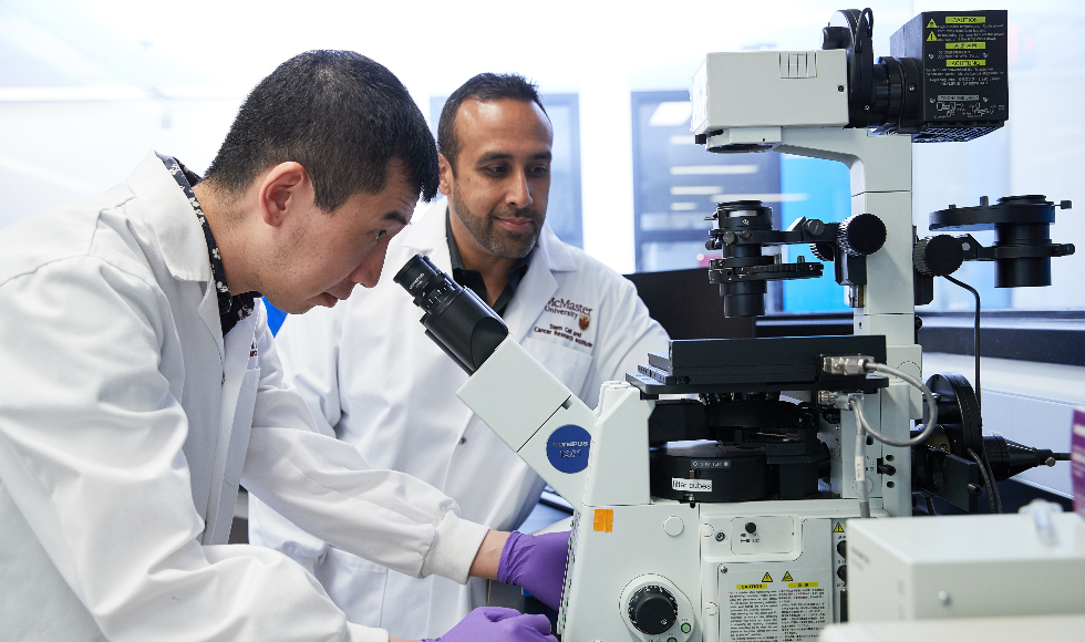 Two men stand over a microscope in a lab