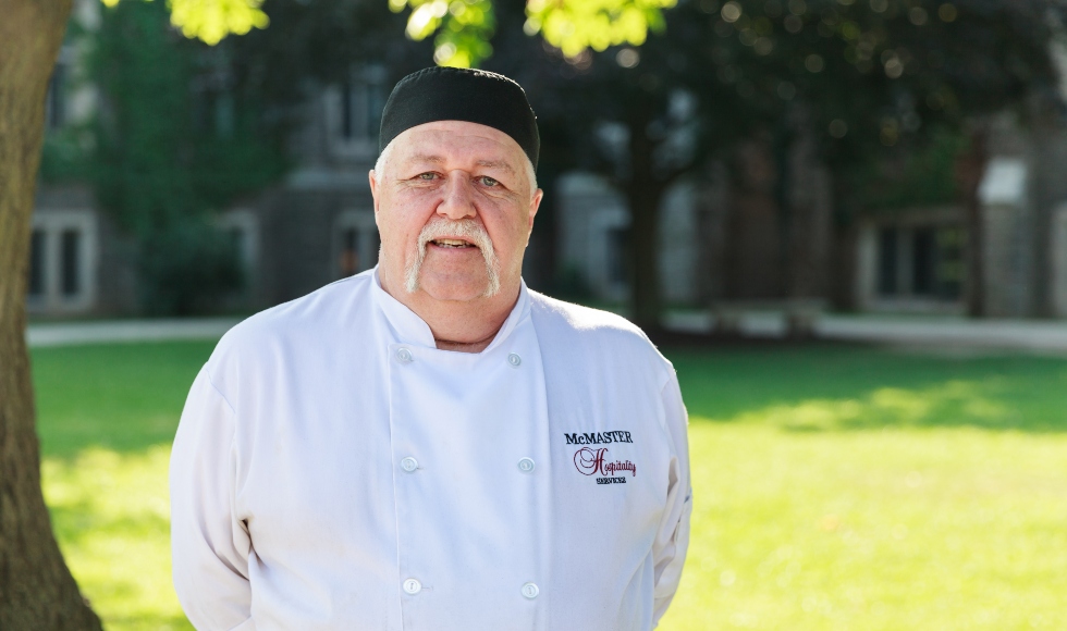 Ray Osborne stands outdoors on campus, wearing his chef uniform