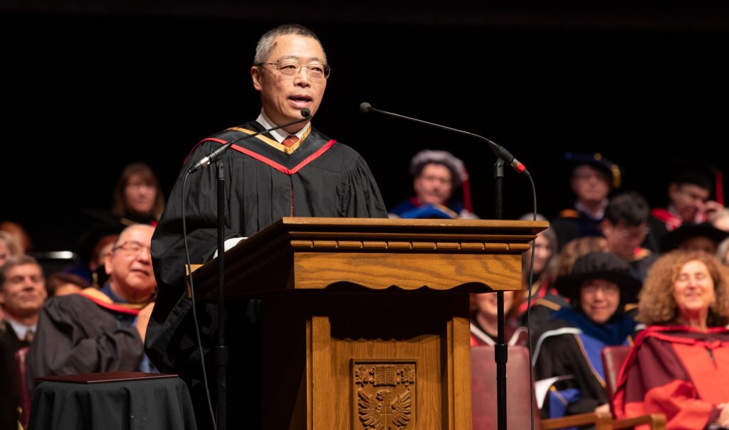 Bruce Miyashita in graduation robe speaks at podium