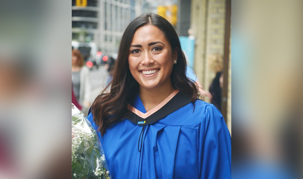 Smiling woman in graduation robe holding a bouquet