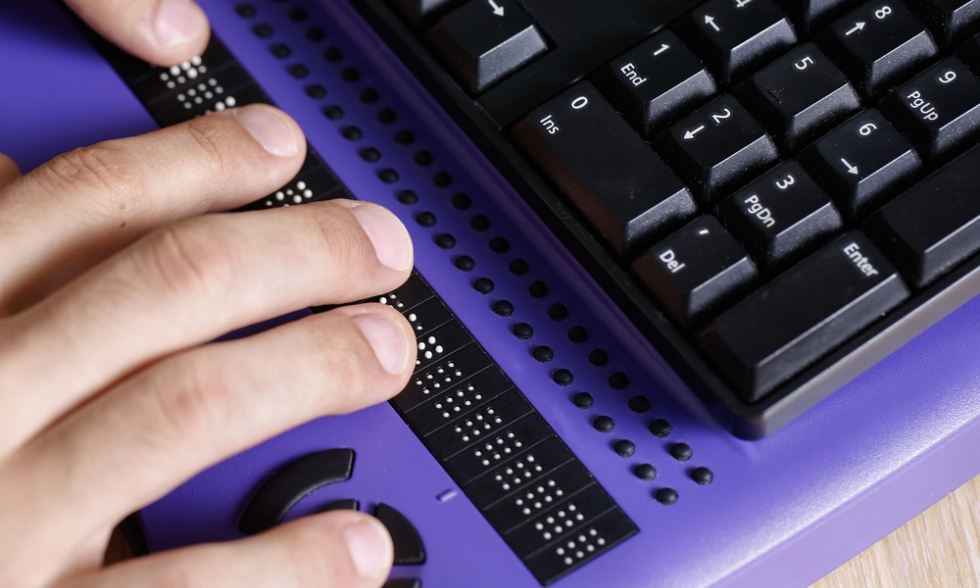 close up Image showing someone typing using braille on a purple keyboard. Only the person's right hand is visible.