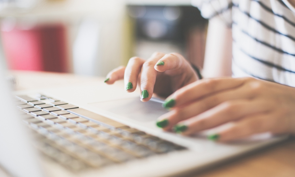 Stock image of a female student with green nail polishing working at her laptop