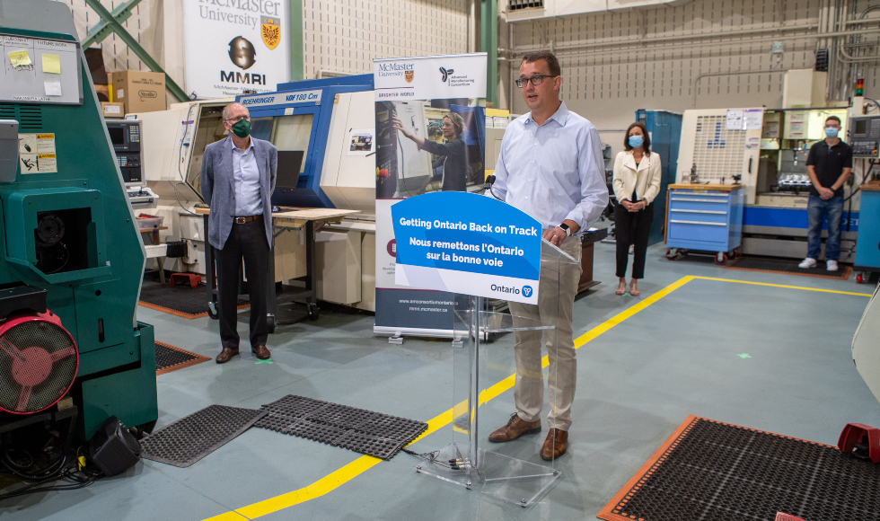 Minister Monte McNaughton stands at a posium in the McMaster Manufacturing Research Institute. President David Farrar and MPP Donna Skelly are in the background.