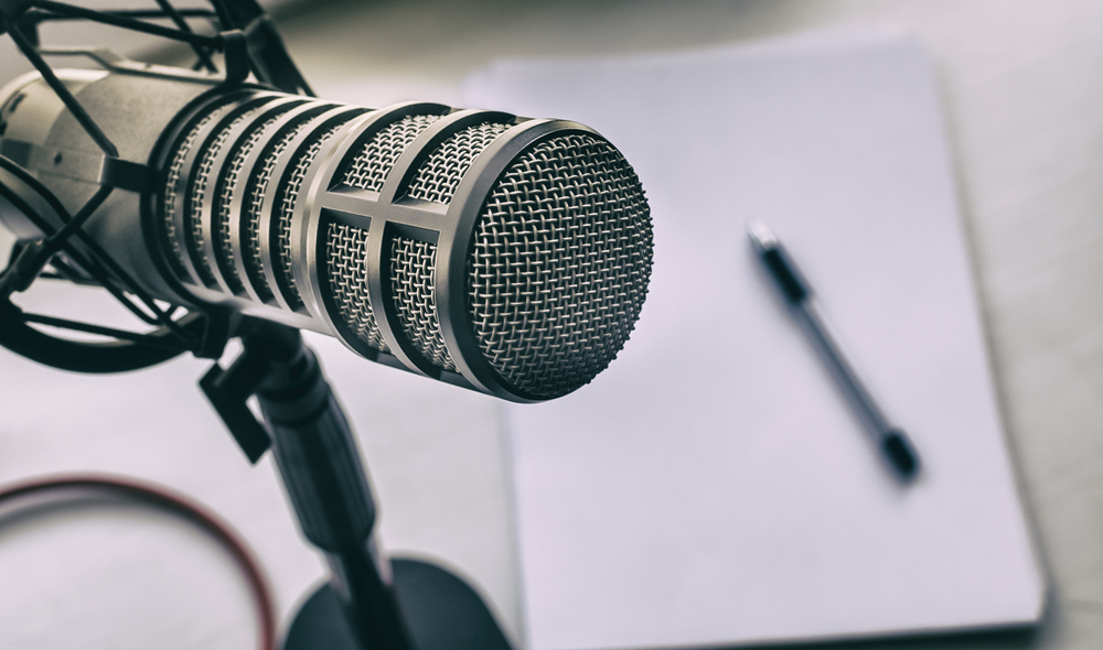 A photo of a microphone sitting on a desk, with a pad of paper and a pen