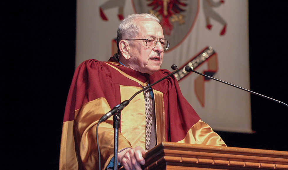 Ronald Bayne in a graduation gown, giving a speech at a podium