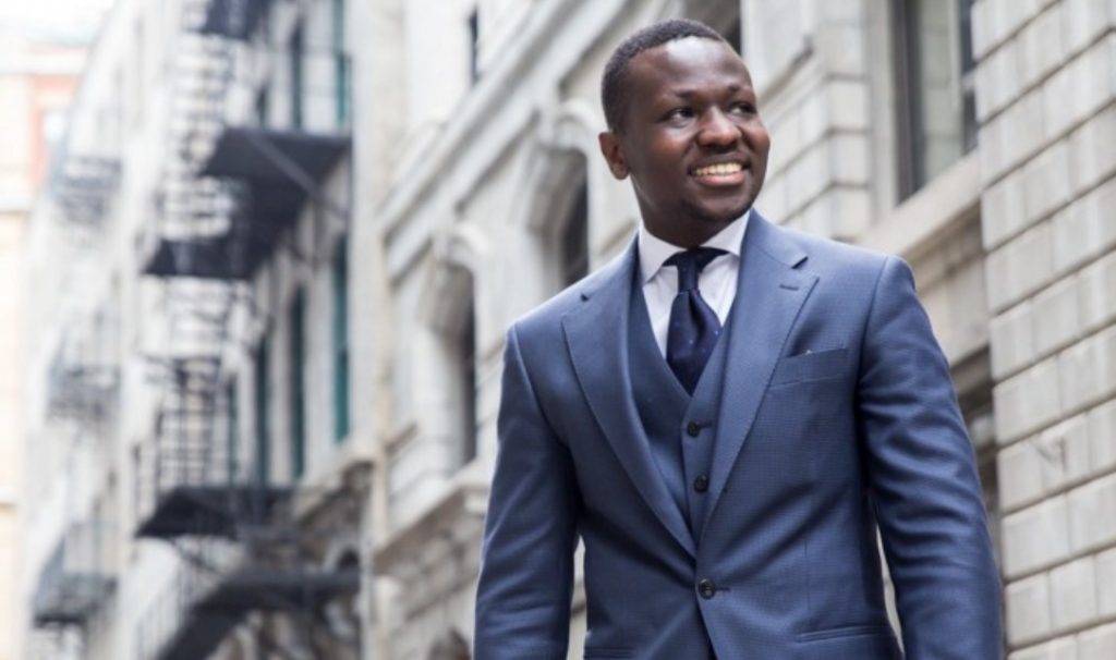 Oghor Collins in a suit, standing in front of a building