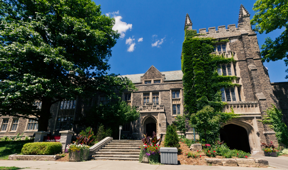 The front of University Hall in the spring, with flowers in beds and pots around the stairs