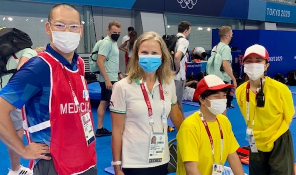 4 masked people in Olympic-branded clothes at an aquatic centre.