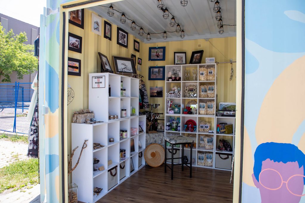 A small gift shop inside a shipping container painted in pastel blue, yellow and purple