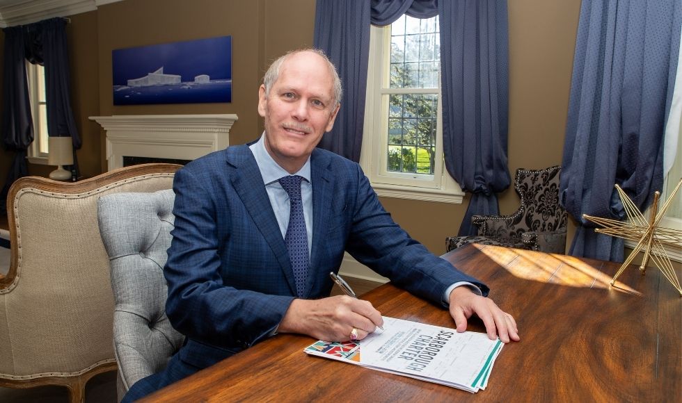 Man in a suit sitting at a desk with papers and a pen. The cover page says 