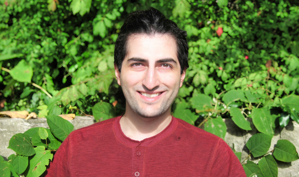 Schulich Leader Seyedbehrad Dehnadi smiles into the camera while sitting outdoors with greenery behind him