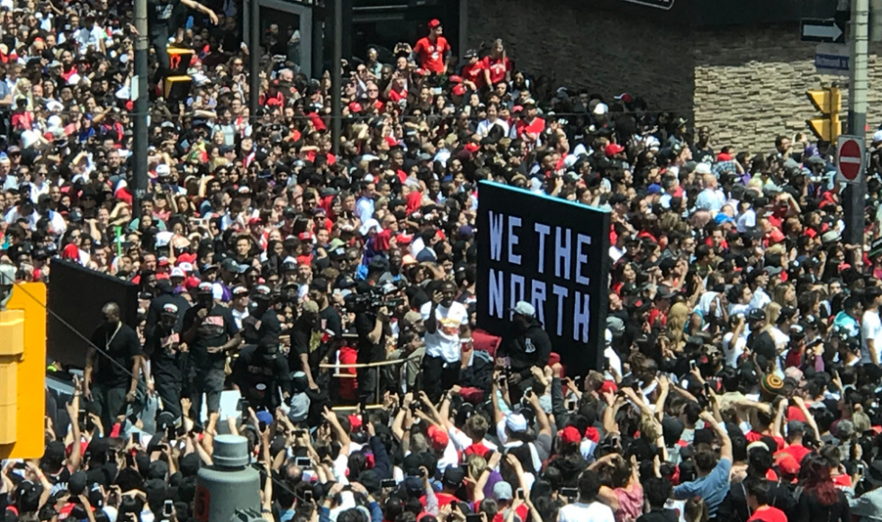 crowd of Raptors fans cheering in downtown Toronto, holding a large 'We the North' sign.