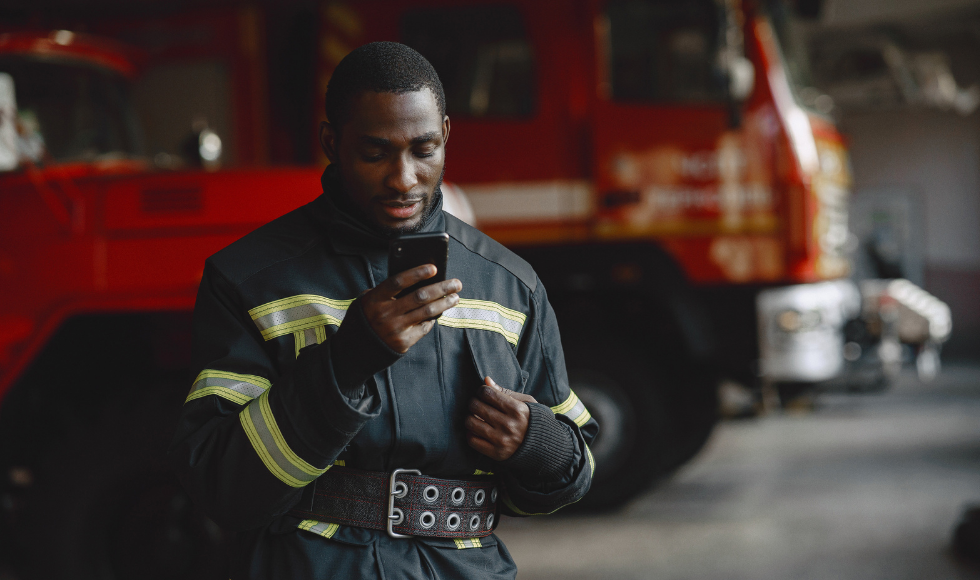 Firefighter in uniform looking at a phone in front of a fire truck.