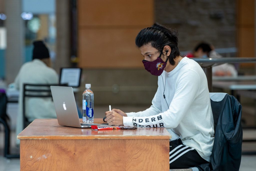student, masked, sits at a desk in the student centre