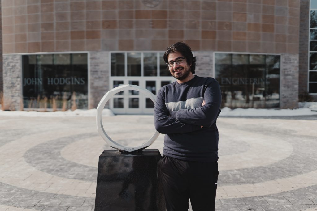 Omar Sabri, 3rd year, electrical engineering co-op stands outside the JHE building, leaning against the iron ring.
