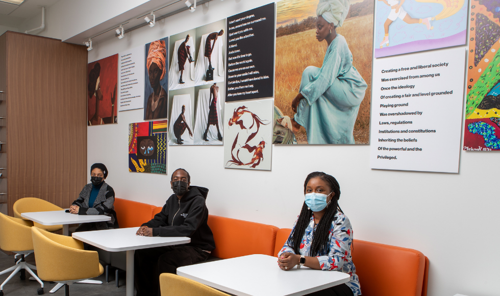 Three people sitting at tables under a wall covered in beautiful art