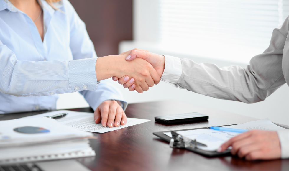 Two people shaking hands at a table covered with documents