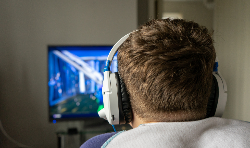 The back of a person's head with headphones on, they are facing a screen with a video game on it.