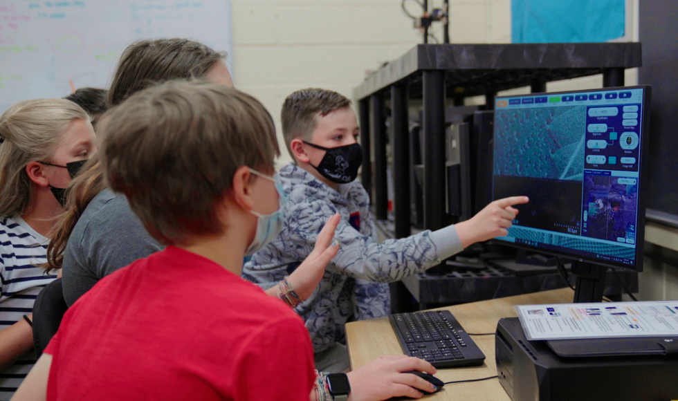 4 students looking and pointing at a monitor with a very magnified image on it.