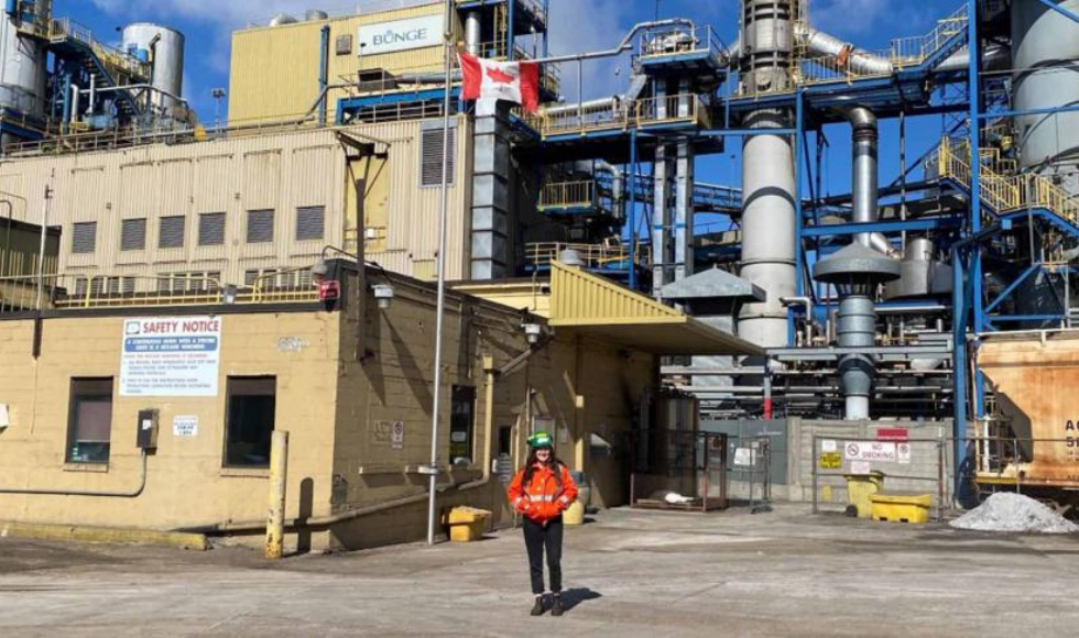 Shayna Earle wearing a hard hat outside a massive industrial building labelled Bunge.